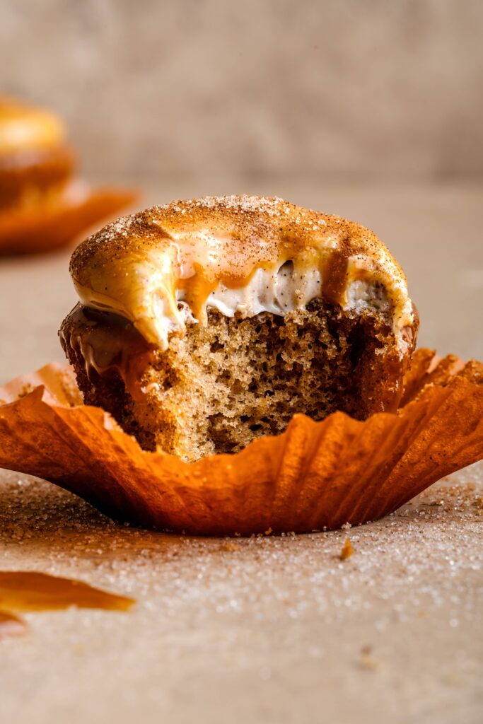 A pumpkin spice cupcake with cream cheese frosting & a caramel glaze, with a bite taken out of it.