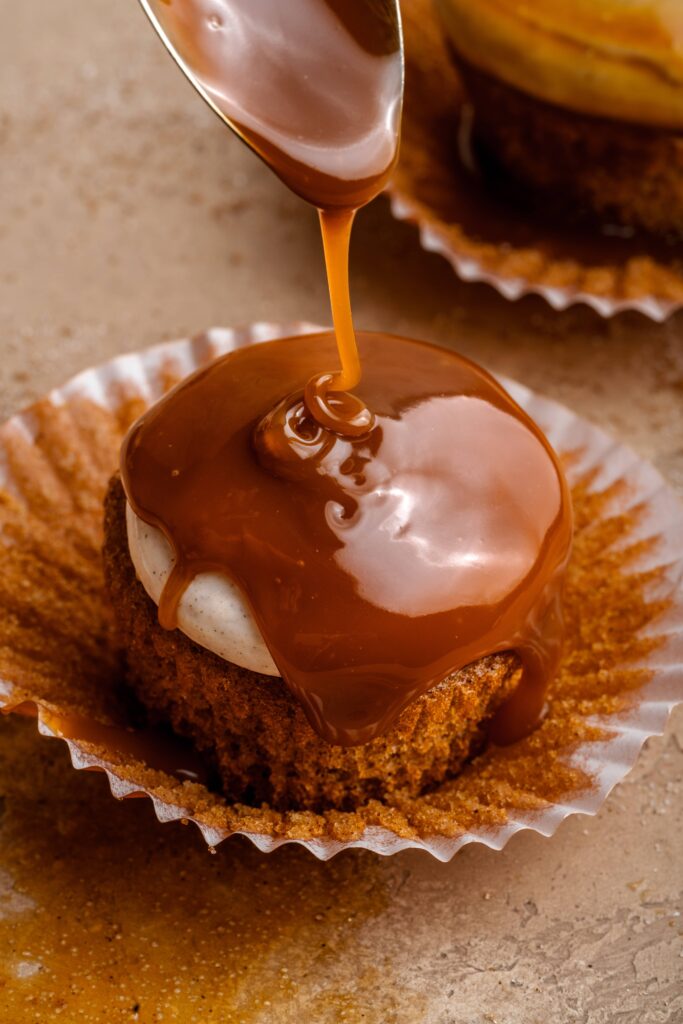 A spice cupcake with cream cheese cinnamon frosting being drizzled with fresh caramel sauce.