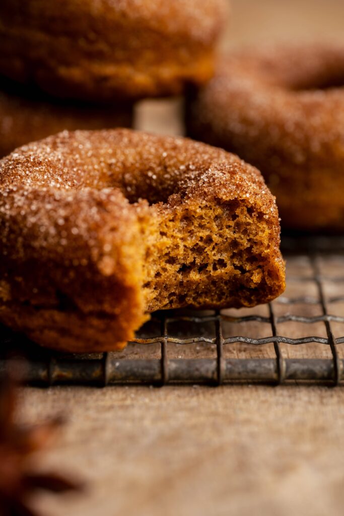 A pumpkin spice donut covered in cinnamon sugar with a bite taken out of it.